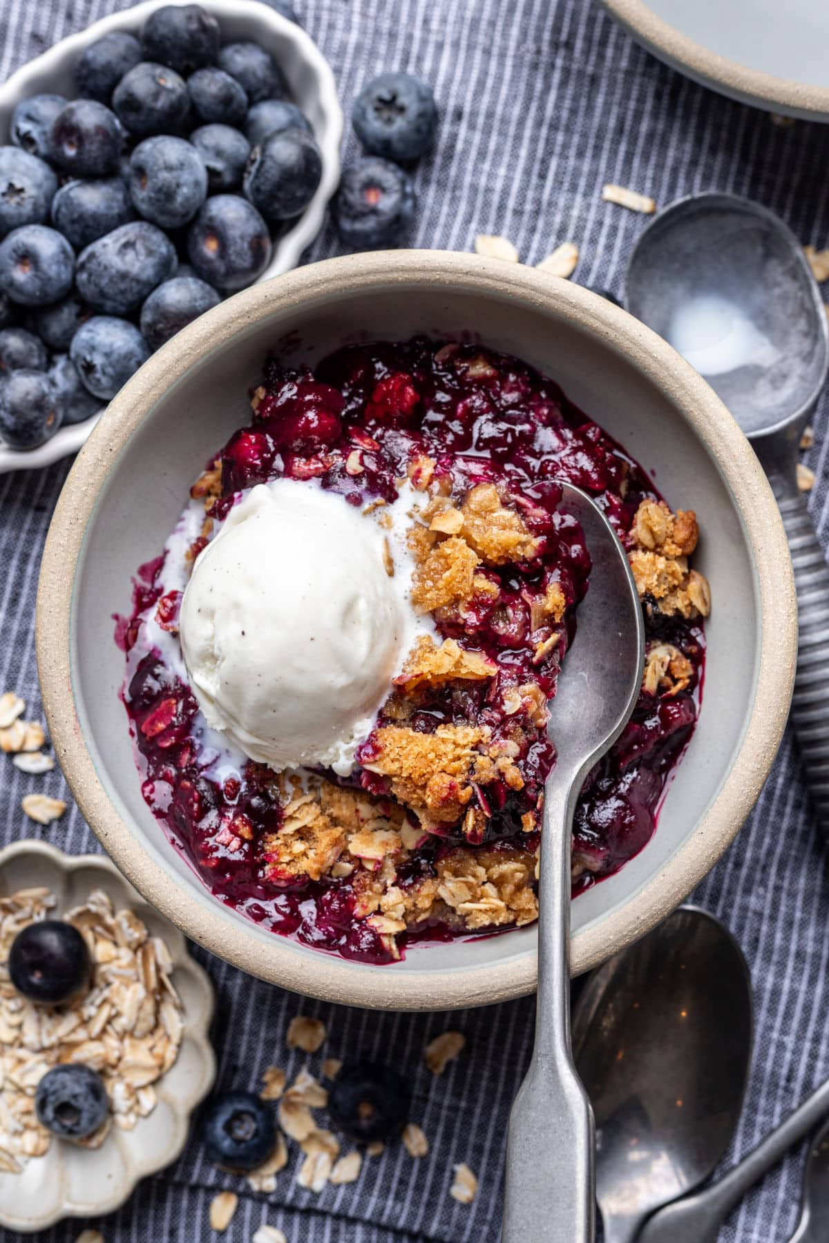 A dish of blueberry crisp topped with a scoop of vanilla ice cream. 