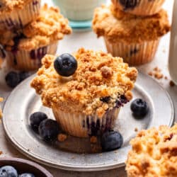 A blueberry streusel muffin with a blueberry on top of it on a plate.