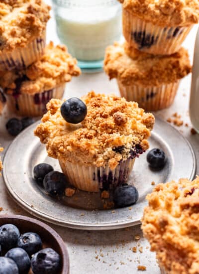 A blueberry streusel muffin with a blueberry on top of it on a plate.