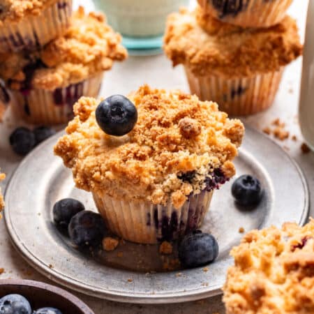 A blueberry streusel muffin with a blueberry on top of it on a plate.