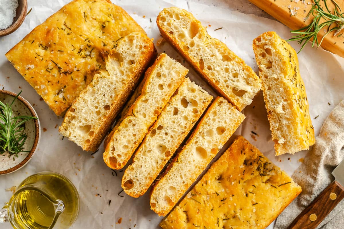 Slices of bread machine focaccia next to dishes of rosemary and olive oil. 