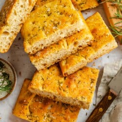Cut pieces of bread machine focaccia next to a knife and a dish of tomato sauce.