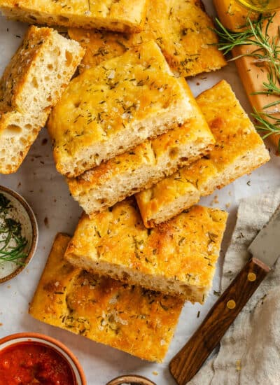Cut pieces of bread machine focaccia next to a knife and a dish of tomato sauce.