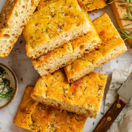 Cut pieces of bread machine focaccia next to a knife and a dish of tomato sauce.