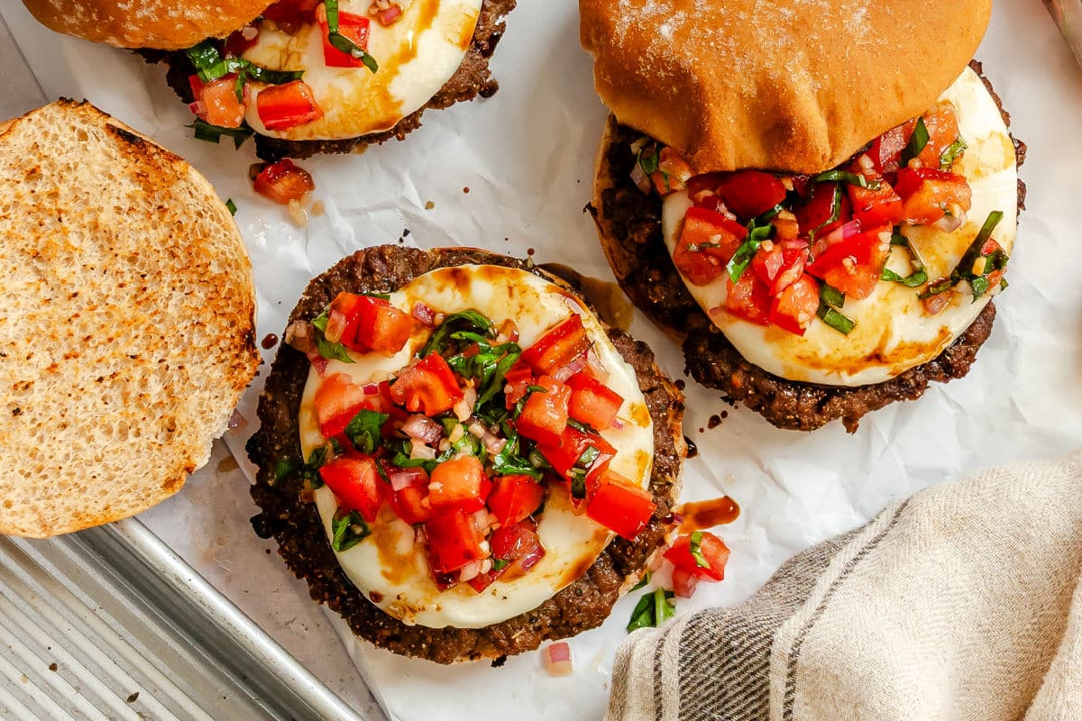 A bruschetta burger with the top bun sitting next to the burger.