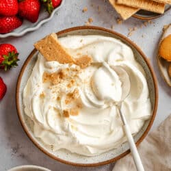 A dish of cheesecake dip with a spoon in it next to a bowl of fresh strawberries.