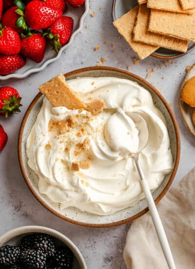 A dish of cheesecake dip with a spoon in it next to a bowl of fresh strawberries.