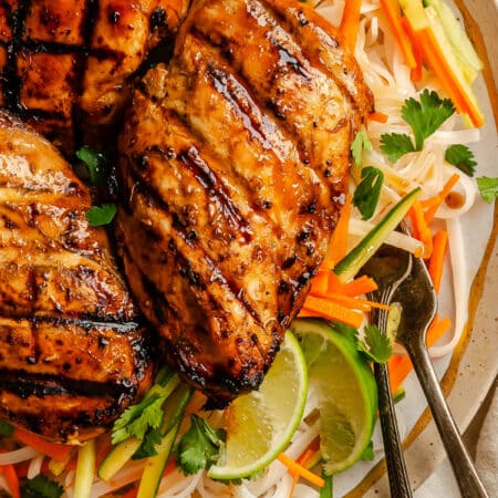 A grilled lemongrass chicken breast on a plate on top of rice noodles.