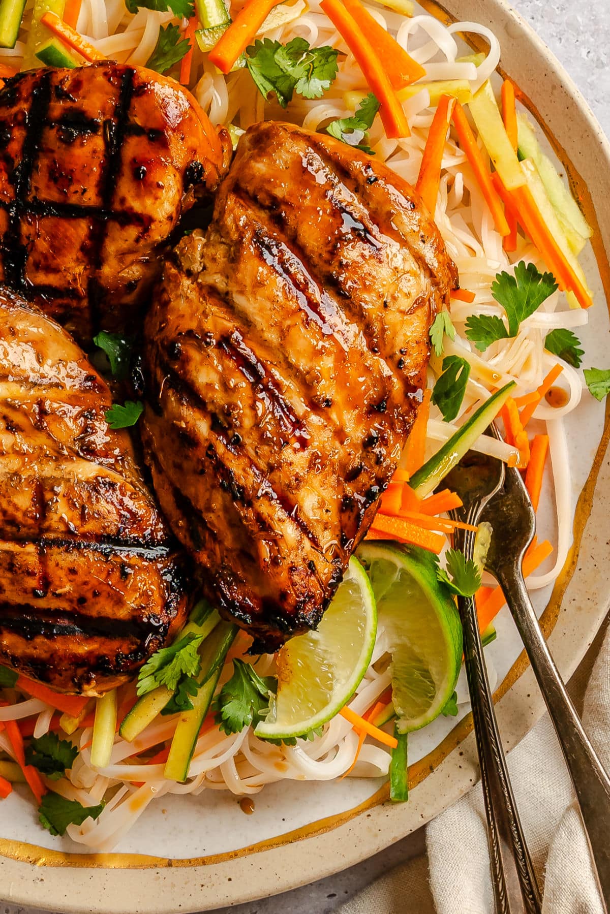 A grilled lemongrass chicken breast on a plate on top of rice noodles.