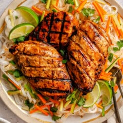 Three lemongrass chicken breasts over rice noodles with julienned vegetables underneath.