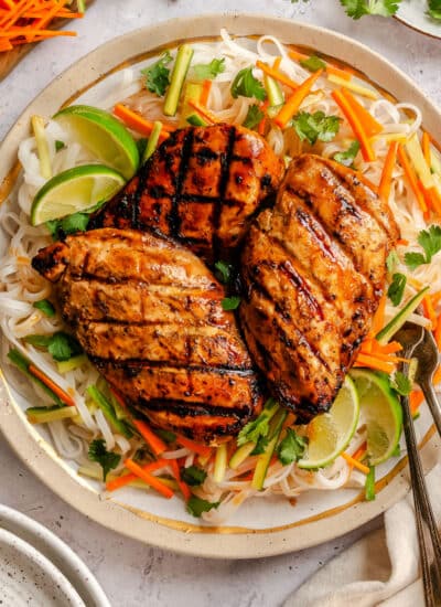 Three lemongrass chicken breasts over rice noodles with julienned vegetables underneath.