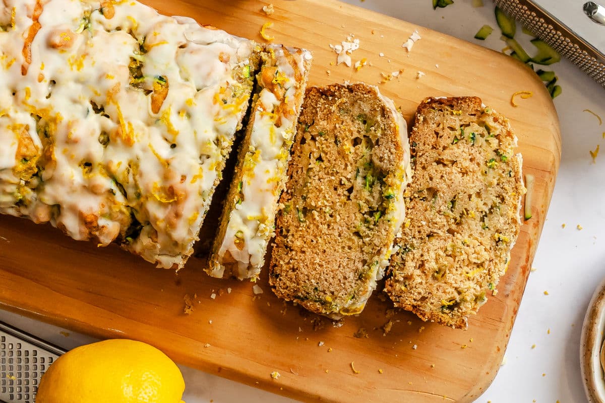 Three slices of lemon zucchini bread next to the loaf on a cutting board.
