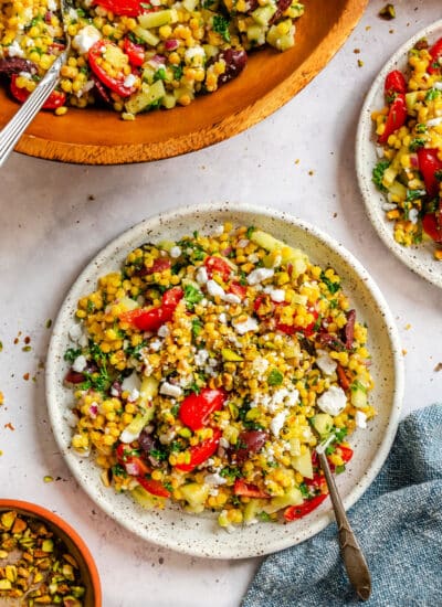 A plate of pearl couscous salad next to the bowl of salad.