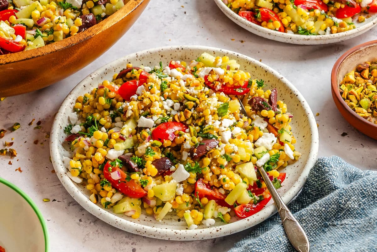 A plate of pearl couscous salad next to the bowl and another plate of salad. 