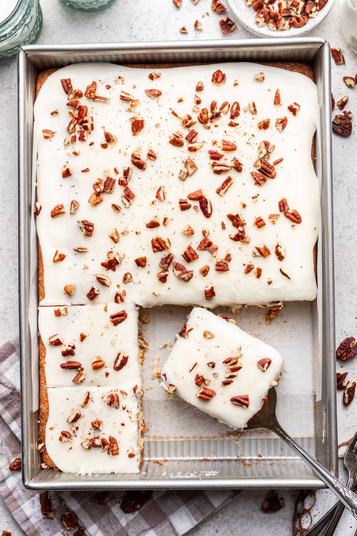 A white Texas sheet cake with pieces missing and a piece on a cake server. 