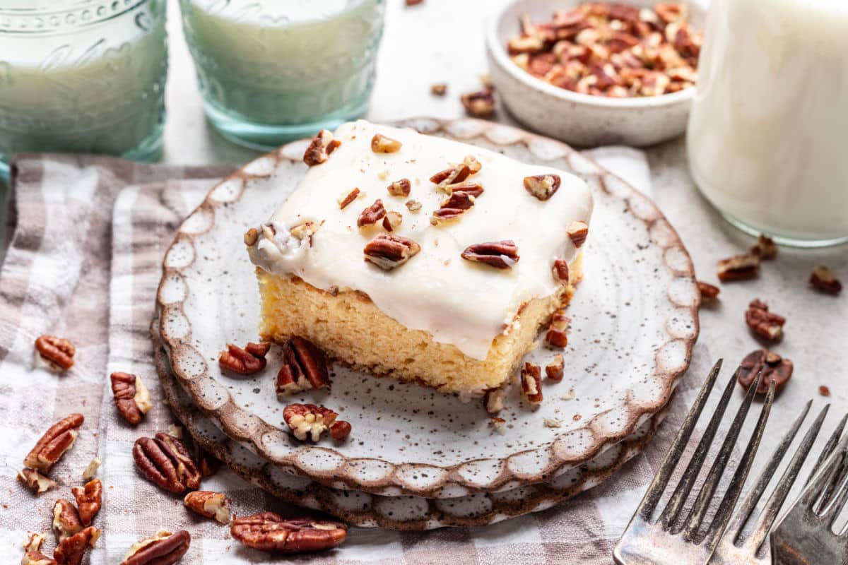 A piece of white Texas sheet cake on a plate next to a glass of milk and a fork. 