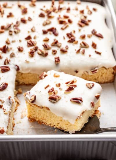 A piece of white Texas sheet cake on a cake server in the cake pan.