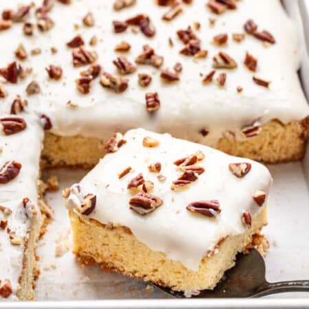 A piece of white Texas sheet cake on a cake server in the cake pan.