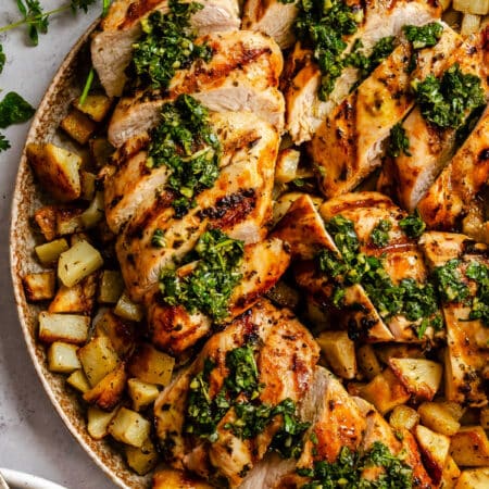 Sliced of grilled chimichurri chicken over roast potatoes.