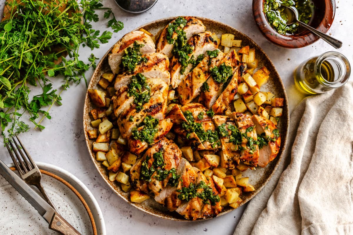 A plate of chimichurri chicken next to a dish of chimichurri sauce.