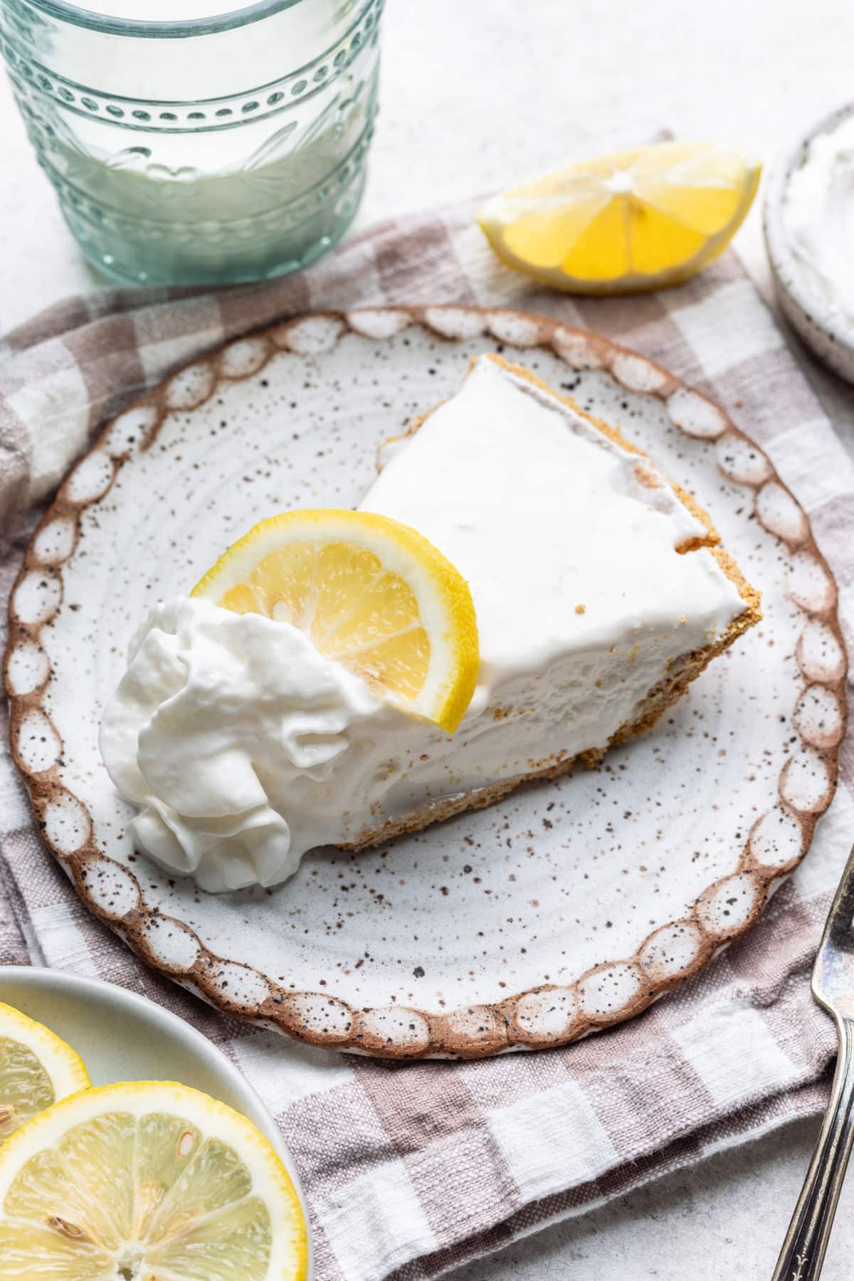 A slice of frozen lemonade pie topped with whipped cream and a slice of lemon.
