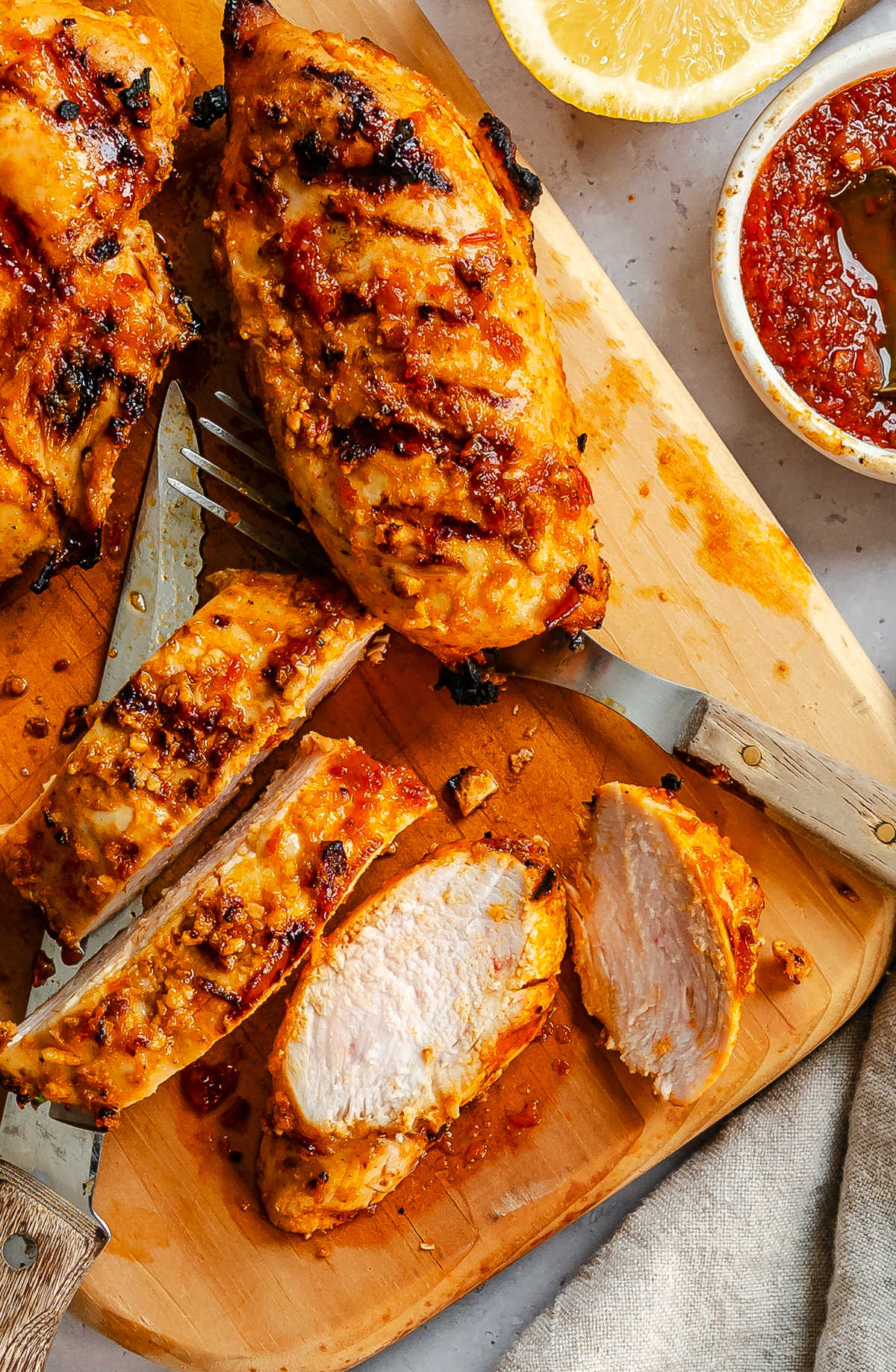 Partially sliced harissa chicken on a wooden cutting board.