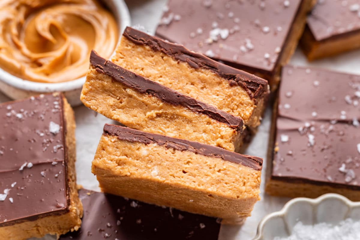 Three sideways no bake peanut butter bars next to a dish of peanut butter.