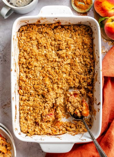 A dish of peach crisp with a spoon holding a scoop.