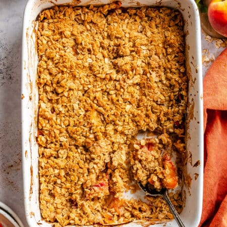 A dish of peach crisp with a spoon holding a scoop.