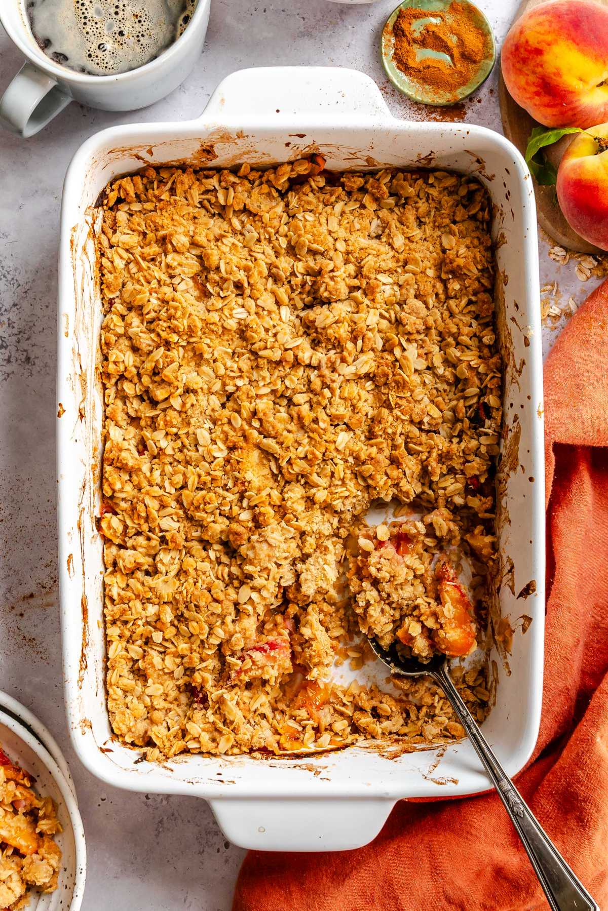 A dish of peach crisp with a spoon holding a scoop.