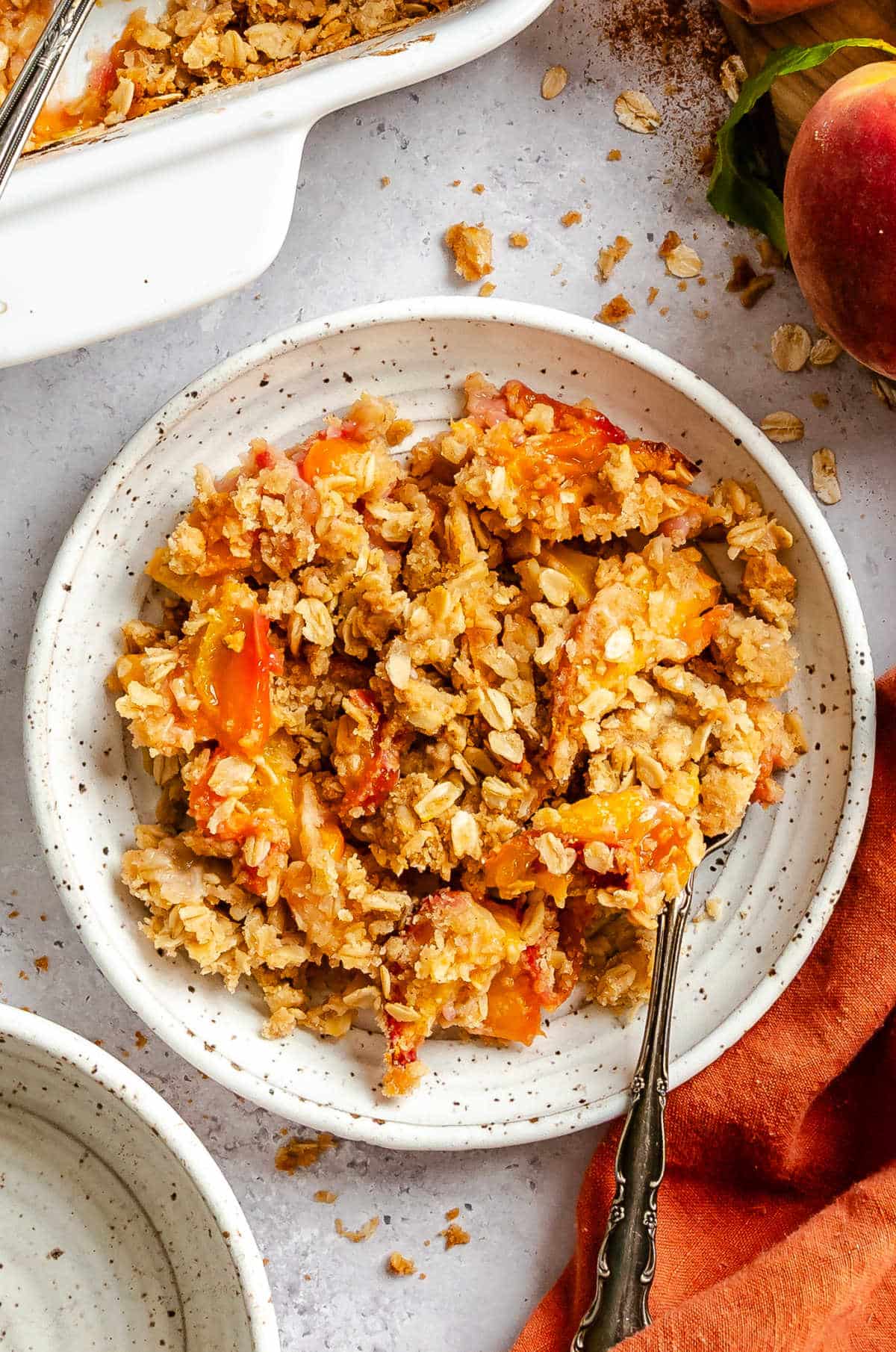 A plate of peach crisp next to the pan of crisp.