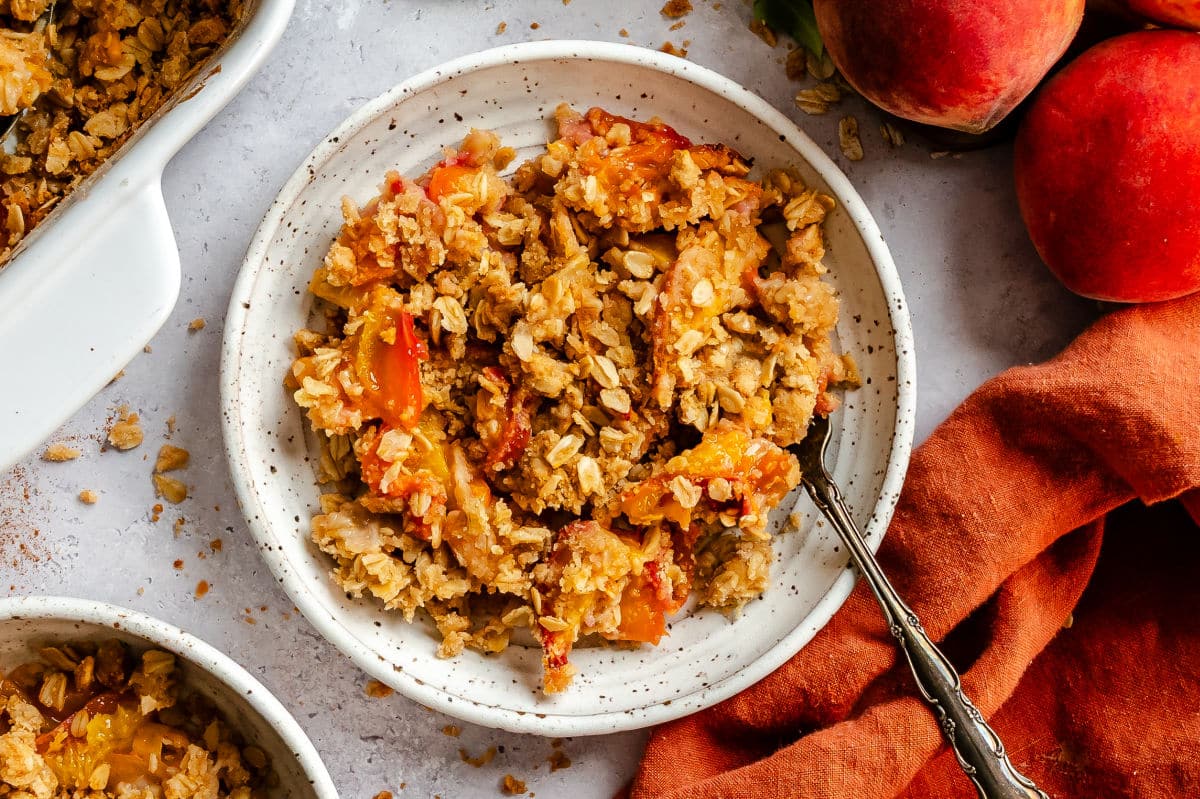 A plate of peach crisp next to an orange kitchen linen.