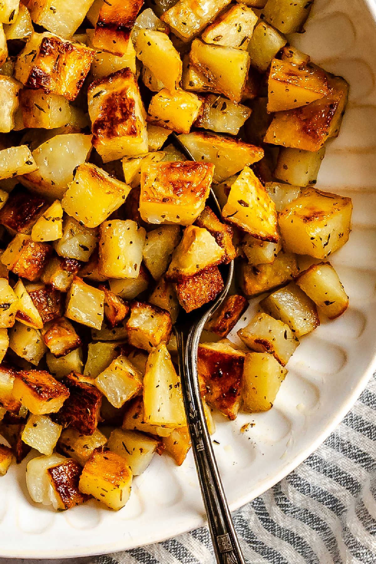 A spoon in a bowl of roast potatoes.