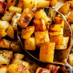 A spoon holding a scoop of roast potatoes.