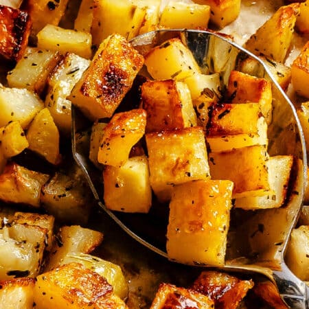 A spoon holding a scoop of roast potatoes.