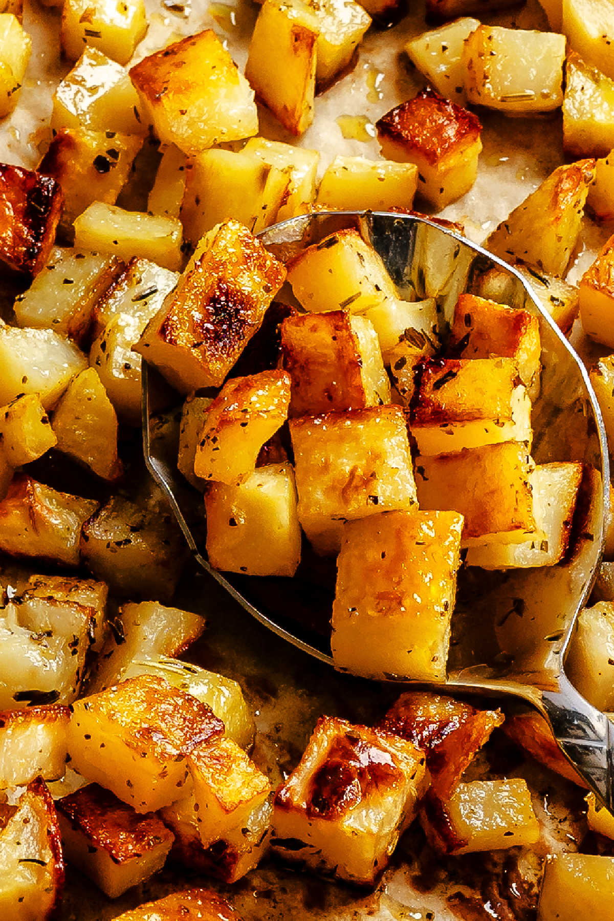 A spoon holding a scoop of roast potatoes.