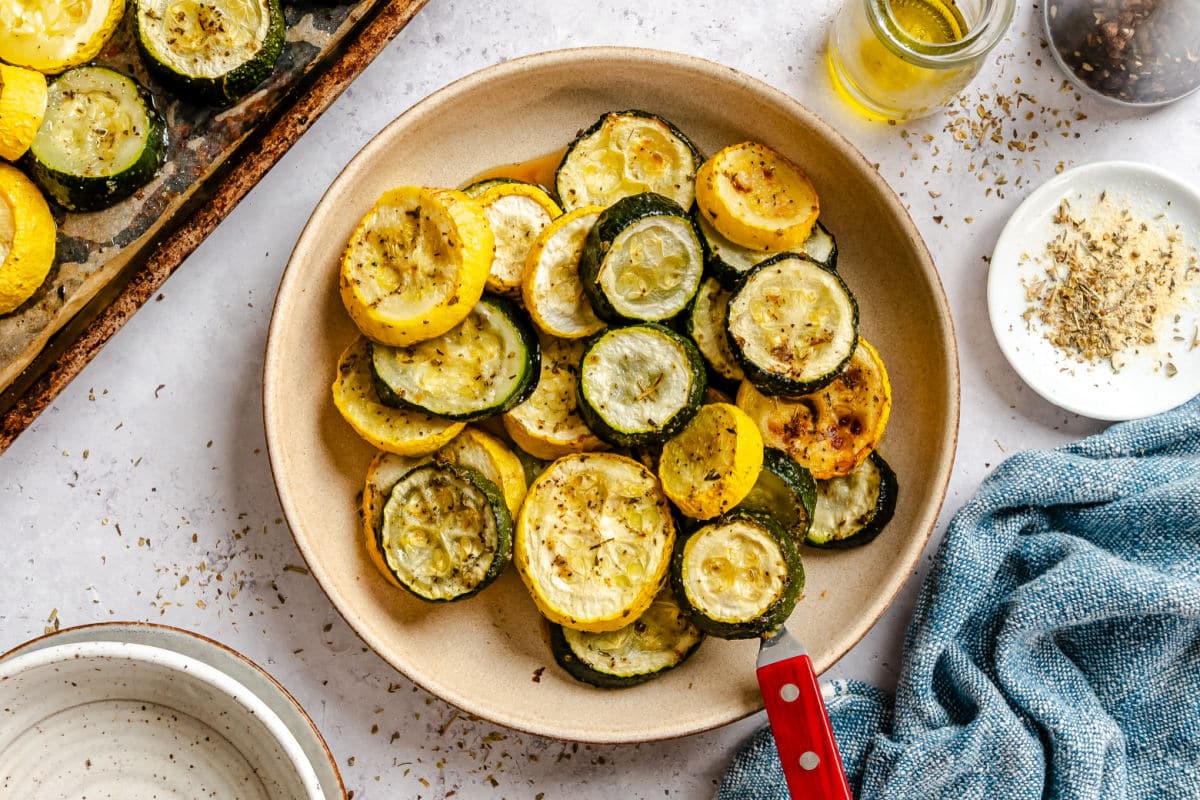 A plate with roasted summer squash and zucchini next to a dish of seasoning.