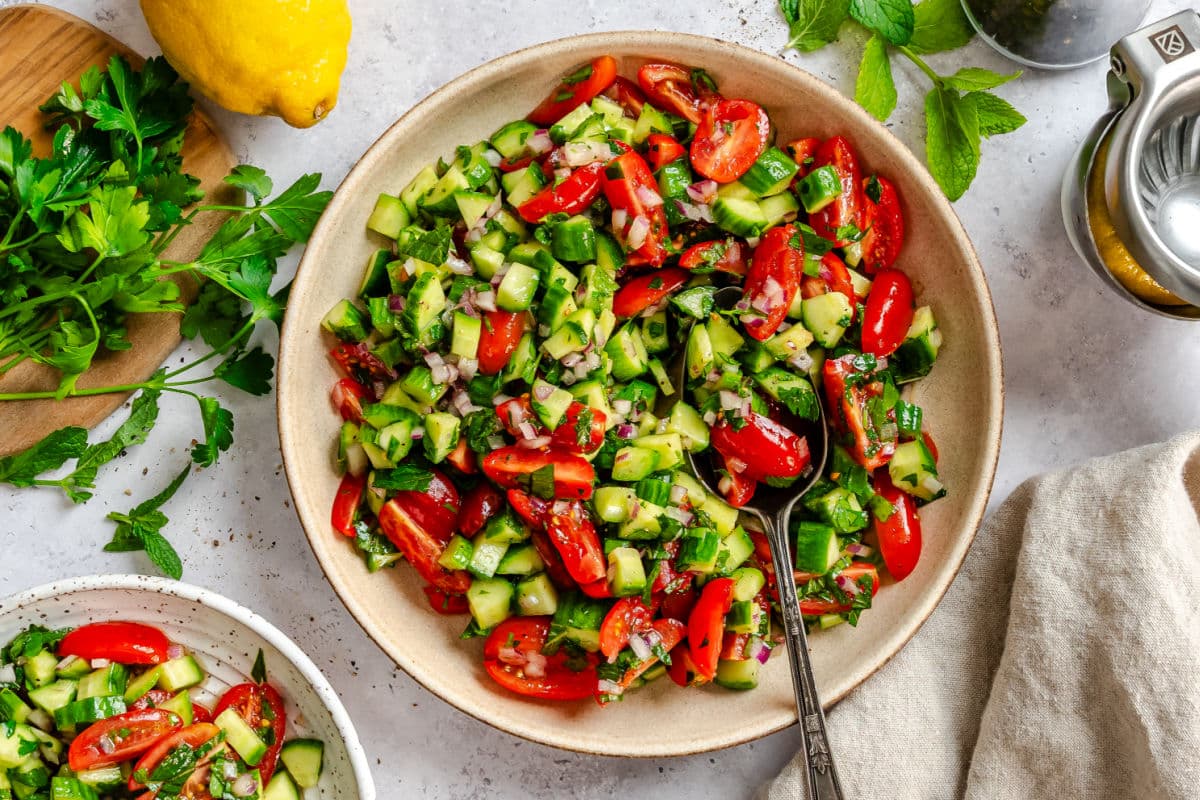 A bowl of shirazi salad next to a juicer and a lemon.
