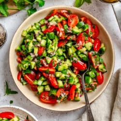 Shirazi salad with a silver spoon in it next to a lemon and a small dish of salad.