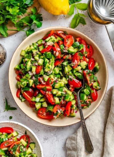 Shirazi salad with a silver spoon in it next to a lemon and a small dish of salad.