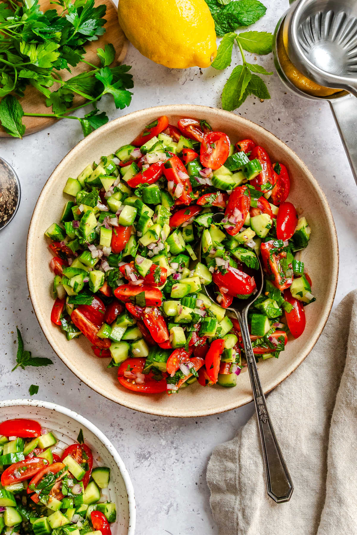 Shirazi salad with a silver spoon in it next to a lemon and a small dish of salad.