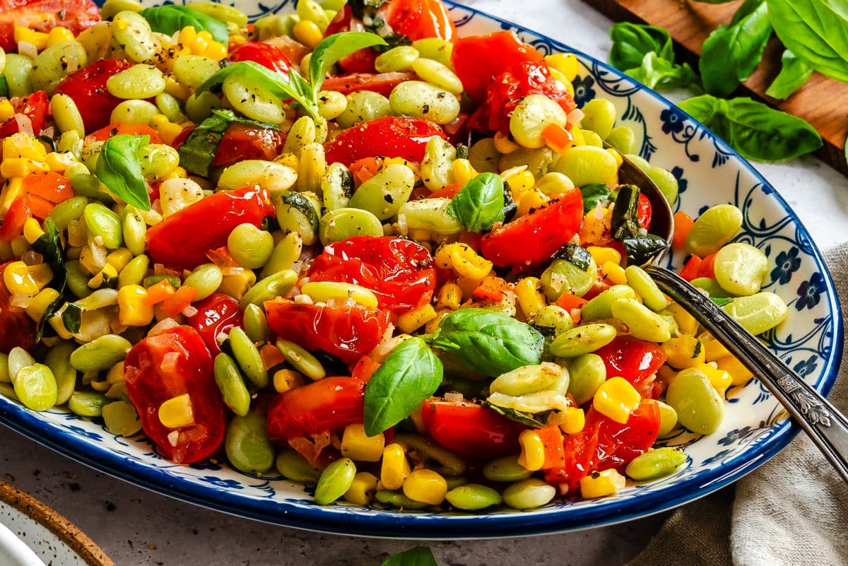 A platter of summer succotash next to fresh basil.