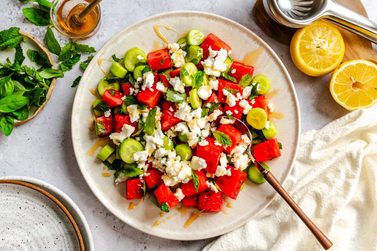 A plate of watermelon feta salad next to fresh basil and mint leaves. 