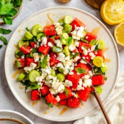 A plate of watermelon feta salad next to a dish of honey and sliced lemons.