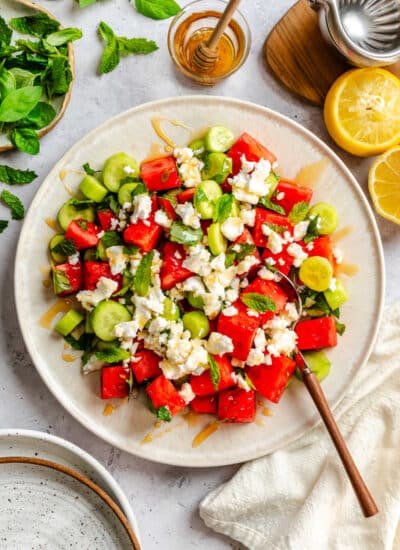 A plate of watermelon feta salad next to a dish of honey and sliced lemons.
