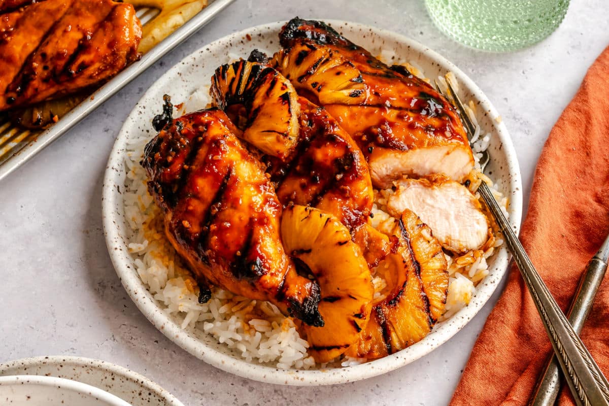 A plate of grilled huli huli chicken with a piece cut.