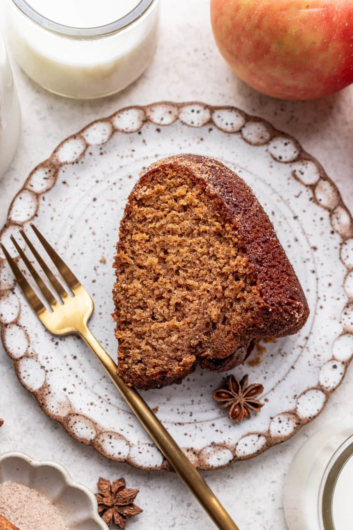 A slice of apple cider cake on a plate with a gold fork next to it.
