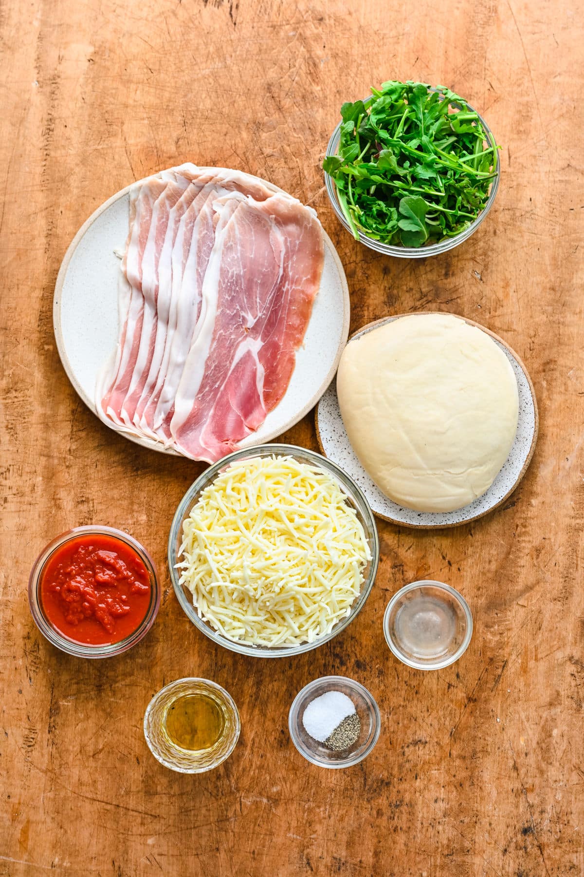 Ingredients for arugula prosciutto pizza in dishes.