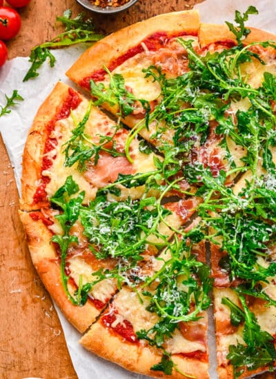 A pizza topped with prosciutto and agrugula.