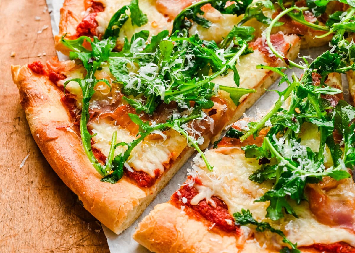 A slice of arugula prosciutto pizza next to the pizza.